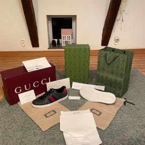Gucci ace skor - Säljer ett par lyxiga Gucci sneakers i svart med klassiskt GG-mönster och vita sulor.  Allt original medföljer. De är storlek 43 och de är helt oanvända .