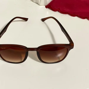 Bruna Ray-Ban solglasögon - Snygga solglasögon från Ray-Ban med brun fyrkantig plastbåge och tonade linser. Modellen är tillverkad i Italien och har diskret Ray-Ban-logga på linsen. Perfekt accessoar för soliga dagar, kommer med svart fodral och putsduk.