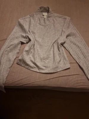 Ljusgrå ribbad tröja från H&M - Säljer en ljusgrå ribbad tröja från H&M i storlek L. Tröjan har lång ärm, hög krage och är tillverkad i mjukt material. Perfekt för lager på lager under höst och vinter. Enkel och stilren design som passar till det mesta. Priset kan diskuteras 🫶