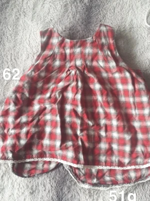 Rutig röd och vit kort klänning - Supersöt kort klänning i rödvitt rutigt mönster. Klänningen är ärmlös och har rundad halsringning samt spetsdetalj längst ner. 🌸 Fint använt skick. Passar fint med en vit body under. Storlek 62