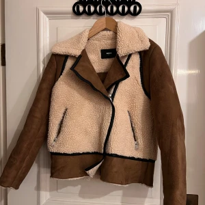 Beige teddyjacka  - Säljer en beige teddyjacka från Bik Bok med bruna mockadetaljer och svarta kantband. Jackan har bred krage, varm och trendig look.