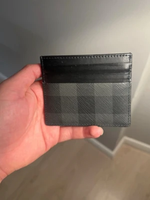 Svart och grå rutig plånbok burberry - Slimmad och stilren plånbok i svart och grått med rutigt mönster. Perfekt för kort och enkel att ha i fickan. Snygg design med flera kortfack och exklusiv känsla.