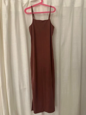Brun långklänning från Monki - Säljer en stilren brun långklänning från Monki i storlek XXS. Klänningen har smala axelband och rak passform som ger en enkel och modern look. Materialet känns mjukt och lätt, perfekt för varma dagar eller lager-på-lager. Passar dig som gillar minimalistisk stil.