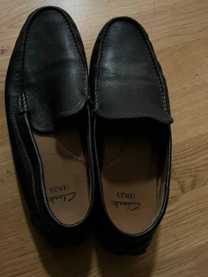 Winter Shoes – Clarks Black Leather Loafers (Comfort & Grip) - High-quality Clarks black leather loafers, perfect for autumn and winter use. Made from genuine leather with a comfortable fit and a durable, non-slip rubber sole, ideal for everyday wear during colder seasons. The shoes are in good used condition, clean and well cared for. Classic and timeless design – suitable for work, school, office, or casual wear. ✔ Warm and comfortable ✔ Slip-on style – easy to wear ✔ Great grip for wet or cold weather ✔ Trusted Clarks quality 