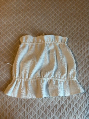 Topp - Supersöt vit kort topp med volangkant och knytband i ryggen. Toppen har  en lätt strukturerad yta och är perfekt för varma dagar. Passar dig som gillar en feminin och trendig stil.