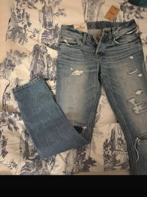 Ljusblå slitna jeans från Hollister - Säljer ett par ljusblå jeans från Hollister med snygga slitningar och hål på benen. Oanvända och as snygga!!