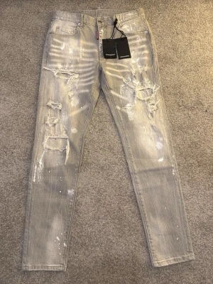 Dsquared2 Jeans - Snygga grå jeans från Dsquared2 med skinny passform och slitna detaljer samt färgstänk för en cool, edgy vibe. Klassisk femficksmodell med Dsquared2 patch bak i midjan. Perfekta för dig som gillar streetstyle och vill sticka ut.