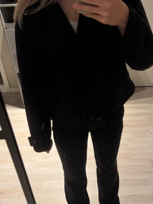 Svart ullkappa med knappar - Säljer en svart kappa i ull med klassisk krage och stora fickor framtill. Jackan har långa ärmar och stängs med en knapp framtill. 