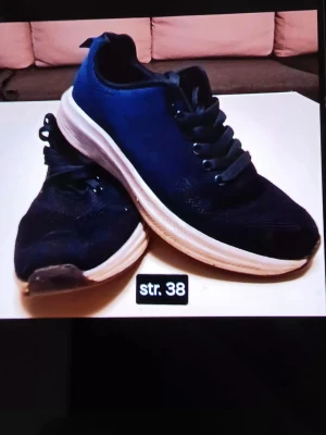 Blå sneakers med vit sula strl 38 - Säljer ett par mörkblå sneakers i storlek 38 med vit sula och svarta skosnören. Skorna har rund tå och är tillverkade i syntetmaterial med meshdetaljer för extra andningsförmåga. Perfekta för dig som gillar en sportig och enkel stil.