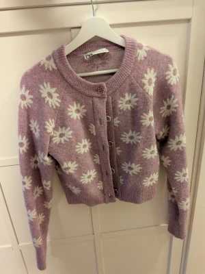 Ljuslila kofta med blommor från Zara!💕💕 - Superfin ljuslila kofta från Zara med vita blommor över hela tröjan. Modell med v-ringning och knappar framtill. Stickad i mjukt material och har långa ärmar. Varm och mysigt material!