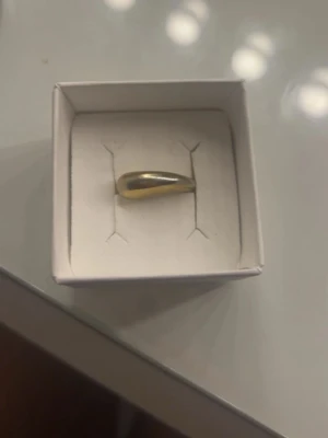 Guldig chunky ring i modern design - Säljer en chunky ring i guldig färg med en modern, droppformad design. Ringen är slät. Perfekt accessoar för dig som gillar statement-smycken och vill sticka ut lite extra. 16 mm