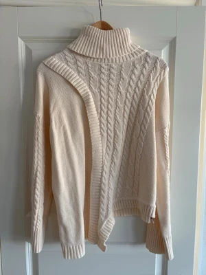 Beige polotröja med kabelstickning M - Säljer en beige polotröja med grov kabelstickning framtill och ribbade detaljer vid hals, ärmslut och nederkant. Tröjan har lång ärm och en loose passform som ger en chill vibe. Perfekt för lager-på-lager under höst och vinter.