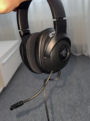 Razer Kraken Gaming Hörlurar  - Razer Kraken är ett kabelanslutet gamingheadset med stor komfort och tydlig mikrofon. Headsetet har över-ear design och USB-anslutning. Skicket ser bra ut med mindre yttre slitage på bågen, inga synliga defekter på kuddar eller mikrofon. Perfekt för spel och kommunikation.