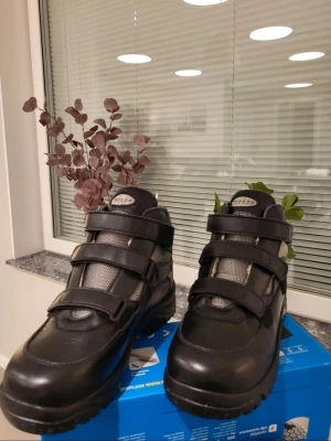 Svarta Chriss boots med kardborre 42 passar 43 - Svarta boots från Chriss med robust sula och tre breda kardborreband för enkel påtagning. Ovandelen är i skinn och textil med grå mesh-detaljer för extra ventilation. Perfekta för dig som vill ha både stil och funktion i vardagen.