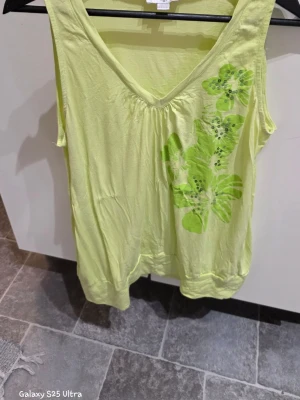 Ljusgul blommig linnetopp - Säljer en ljusgul linnetopp från Halens i storlek 44/46. Toppen har v-ringning och är ärmlös med gröna blommor tryckta på ena sidan. Materialet är mjukt och lätt bomull, perfekt för varma dagar. Passformen är loose och toppen har ett avslappnat fall.