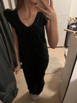 Svart blus med v-ringning och volang - Säljer en svart blus med v-ringad hals och korta volangärmar. Blusen har ett diskret rutmönster i tyget som ger en snygg struktur.💞