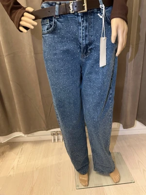 Blå prickiga jeans från Zara - Snygga blå jeans från Zara med små vita prickar över hela tyget som ger en unik look. Modellen har normal passform och raka ben, klassisk femficksdesign och hög midja. Materialet är robust denim i bomull. Perfekt för dig som vill sticka ut med detaljer.