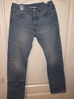 Levi's 501 ljusblå jeans - Ljusblå Levi's 501 Premium jeans med klassisk femficksdesign och raka ben. Jeansen har hög midja och är tillverkade i bomull med snygga kontrastsömmar. Perfekt för dig som gillar tidlös denimstil och vill ha ett par ikoniska jeans i garderoben.