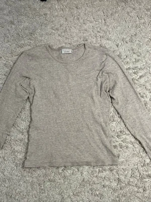 Beige ribbad långärmad topp Kappahl  - Säljer en beige ribbad långärmad topp från Sinclair by Kappahl. Toppen har en rund halsringning och är i ett mjukt, stretchigt material.
