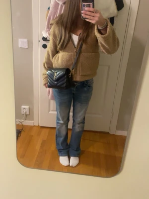 Beige teddyjacka med dragkedja - Mysig beige teddyjacka med dragkedja framtill och stora fickor. Jackan har en avslappnad passform och är perfekt för kyligare dagar. Tillverkad i fluffigt teddy-material som ger en trendig och bekväm look. Långärmad och lätt att matcha med olika outfits.