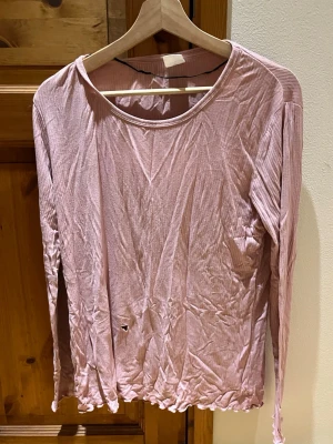 Rosa långärmad tröja - Rosa, tunn, ribbad långärmad tröja. Väl använd med ett litet hål på magen. Har använts som sovtröja vilket fungerade super. Väldigt skönt material i min syn. Bild på slitage finns med. Tyget kan upplevas något nopprigt. Är i storlek S 36/38 från Serenity. Säljes då den inte kommer till användning. Djur och rökfritt hem.
