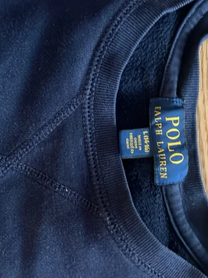 Mörkblå sweatshirt från Polo Ralph Lauren - Snygg mörkblå sweatshirt från Polo Ralph Lauren med klassisk röd broderad logga på bröstet. Tröjan har rund hals, långa ärmar och är gjord i mjuk bomull.  Passar de som är ungefär 165 långa.  Storlek large i barnstorlek. Passar de som uppskattningsvis de som är mellan 14-16 år.