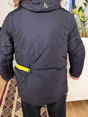 Parajumpers mörkblå parkajacka L - Säljer en mörkblå Parajumpers parkajacka med gul detalj och patch på ärmen. Jackan har pälskantad huva, flera fickor, dragkedjor och knappar framtill. Materialet är slitstark polyester och jackan är perfekt för kalla dagar. Stora fickor och coola detaljer gör den riktigt snygg. Pälsen går att ta av . Priset går att diskutera