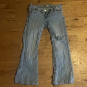 Bootcut &lowaist Jeans från Gina tricot  - Säljer ett par ljusblå bootcut jeans från Gina Tricot i storlek L 14+. Jeansen har klassisk femficksdesign, slitning med hål på ena knät och snygga broderade detaljer på bakfickorna. Perfekt för dig som gillar en avslappnad och trendig look.dom här andvändts men i bra skick.