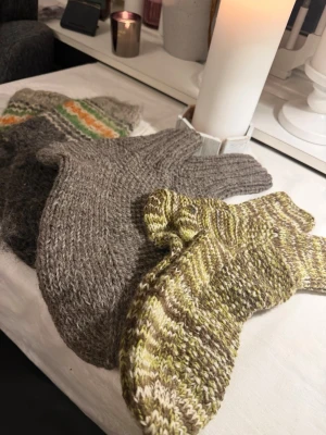 Stickade ullsockor i olika färger - Tre par stickade ullsockor säljes! Ett par är gråmelerade, ett par har mönster med grönt, orange och vitt, och ett par är randiga i grönt, brunt och beige. Alla är tjocka och ribbstickade vid skaftet, perfekta för kalla dagar. Storlek 30,36,38,39,44