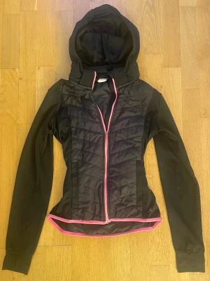 Träningsjacka - Snygg svart jacka med huva, perfekt för kyliga dagar. Jackan har en rosa dragkedja och rosa kant nedtill. Säljer pga den ej kommer till användning! Kontakta vid frågor💗Stolek 158 men sitter som Xs!