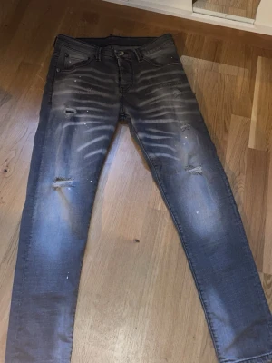 DSQUARED2 skinny jeans med slitningar - Snygga mörkgrå skinny jeans från DSQUARED2 med slitna detaljer och coola blekta ränder framtill. Baksidan har broderad text på fickan och läderpatch i midjan. Jeansen har stänk och slitningar för en edgy vibe. Perfekt för dig som gillar streetstyle. Den passar för dom som har Storlek S/M