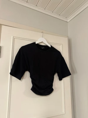 Svart croppad t-shirt Gina Tricot - Svart croppad t-shirt från Gina Tricot i storlek XS. T-shirten har korta men luftiga ärmar och är tight vid midjan. Säljer för att den tyvärr inte kom till användning så mycket eftersom jag har en liknande i en annan färg.