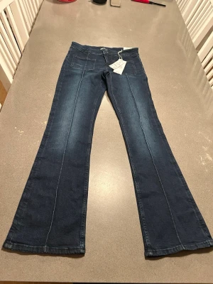 Nya Pleated flare jeans low waist Gina Tricot Young 170 - Nya med prislapp. Storlek 170, passar XS. Flare jeans från Gina Tricot Young med låg midja. Jeansen är blåa och har utsvängda ben med normallängd. De har normal passform, låg stretch, veck framtill och fickor fram och bak.