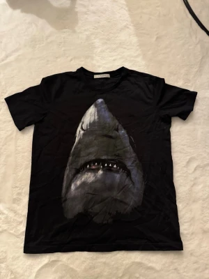 Givenchy shark print tshirt  - Skick: mycket bra, inga fläckar / hål Detaljer: 	•	Färg: svart med tryck på framsidan 	•	Material: bomull 	•	Passform: regular fit 	•	storlek: S (Passar medium)  Plagget kommer från rök- och djurfritt hem.  📦 Frakt: skickas samma dag om köp går igenom innan 18.00 💬 Frågor: Hör av dig om du vill ha fler bilder eller mått 🤝 Paketpris: Samfraktar gärna vid flera köp 