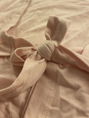 Ljusrosa omlottopp från Gina Tricot - Supersöt ljusrosa omlottopp från Gina Tricot i mjuk bomull. Toppen har långa ärmar och knytdetalj i sidan som ger en snygg och avslappnad look. Perfekt att styla med jeans eller kjol för en chill vibe.💗