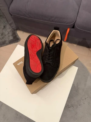 Svarta sneakers från Christian Louboutin - Säljer ett par svarta sneakers från Christian Louboutin i mocka med den ikoniska röda sulan och signaturdetalj undertill. Skorna har snörning och en stilren, rund tå. Kommer med originalkartong och äkthetsbevis. Perfekta för dig som vill ha något exklusivt och tidlöst.