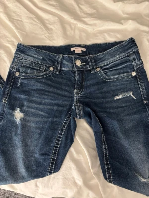 Lågmidjade blå jeans med slitningar från Gina Tricot - Säljer ett par mörkblå jeans från Gina Tricot med snygga slitningar och kontrastsömmar. Jeansen är väldigt lågmidjade. Jeansen har broderade bakfickor och klassisk femficksdesign. Materialet är jeans med stretch och passformen är normal. De har bara användts ett fåtal gånger och det finns inga tecken på användning! Skicka om ni vill ha fler bilder eller har frågor!!💗