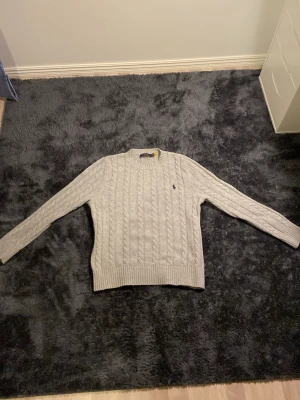 Ljusgrå kabelstickad tröja Polo Ralph Lauren - Säljer en ljusgrå kabelstickad tröja från Polo Ralph Lauren. Klassisk rund halsringning, långärmad och logotyp i blått på bröstet. Perfekt nu för vintern och för den kommande våren. Tveka inte på att höra av er vid funderingar och pris!!