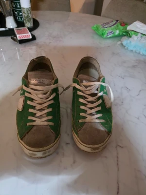 Gröna Philippe Model sneakers - Säljer ett par gröna Philippe Model sneakers med vita detaljer och snörning. Skorna har beige mocka på tå och häl, samt en silverfärgad detalj på sidan. Klassisk låg modell med platt sula och rund tå. Perfekta för dig som gillar en sportig och avslappnad stil.