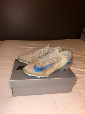 Nike Vapor 16 Elite FG fotbollsskor - Säljer ett par Nike ZM Vapor 16 Elite FG i färgen Glacier Blue/Blue Orbit. Skorna har en snygg blå Nike swoosh på sidan, snörning och en lätt ovandel i syntetmaterial. Sulan har Air Zoom-dämpning och dobbar för spel på naturgräs. Perfekta för dig som vill ha grym touch och speed på planen.