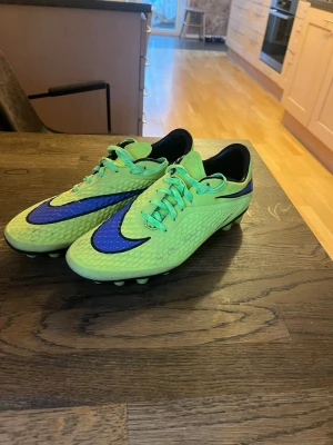Nike Hypervenom fotbollsskor limegrön - Säljer ett par Nike Hypervenom fotbollsskor i limegrönt med blå detaljer och svart sula. Skorna har snörning, mönstrad ovansida och klassiska dobbar för konsgräs. Perfekta för dig som vill sticka ut på planen med snygg design och grym passform.