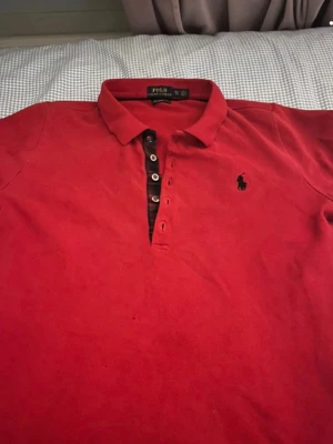 Röd pikétröja från Ralph Lauren S - Säljer en klassisk röd pikétröja från Polo Ralph Lauren i modellen The Skinny Polo. Tröjan har krage, knappar framtill och den ikoniska broderade loggan på bröstet. Tillverkad i 100% bomull för en skön och luftig känsla.