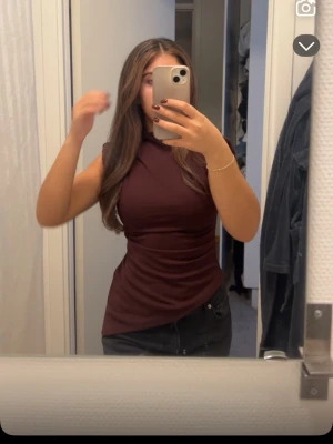 Mörkröd ärmlös topp - Säljer en snygg mörkröd ärmlös topp med hög hals och figurnära passform. Toppen har en stilren design utan mönster och är perfekt att matcha med jeans eller kjol. Materialet känns mjukt och stretchigt, vilket gör den bekväm att bära hela dagen.