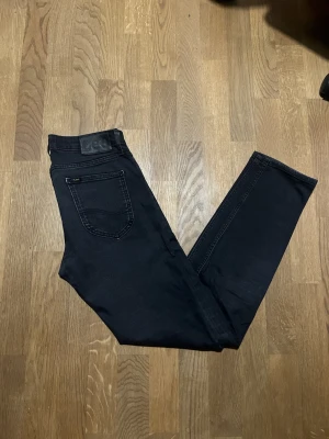Svarta skinny jeans från Lee Malone - Säljer ett par svarta skinny jeans från Lee med klassisk femficksdesign och diskret Lee-logga på bakfickan. Jeansen har smal passform och är tillverkade i stretchigt bomullsmaterial för extra komfort. Perfekta till sneakers eller boots.