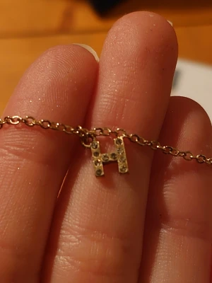 Guldfärgat halsband med H-berlock - Snyggt halsband i guldfärg med en liten H-berlock dekorerad med glittrande stenar.☺️💕