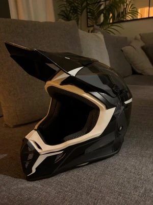 moped/ crosshjälm - Säljer en vit/svart crosshjälm i bra skick. Hjälmen har mjuk fodring inuti som gör den bekväm även vid längre körning, samt ett fungerande spänne/knäppe under hakan som är lätt att justera och känns stabilt.  Hjälmen är E1-märkt och lagligt godkänd, så den får användas i trafik.  Storlek är L – uppskattningsvis 59–60 cm. Passar för cross, enduro eller moped/MC med crossstil.