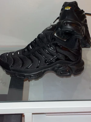 Nike Air Max Plus TN helsvarta sneakers - Helt nya utan box Nike Air Max Plus TN sneakers i helsvart med mesh och syntetpaneler, ikoniska vågmönster och synlig Air-enhet i sulan. Skorna har snörning, Tn-logga bak och en chunky, sportig vibe som sticker ut. Perfekta för dig som gillar streetwear och vill ha något som syns.