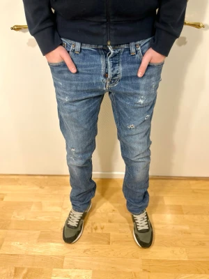 Nudie jeans Grim Tim - slim fit med snygg fade och slitage - Rikigt feta jeans. Jeansen är i blå/ljusblå demon med tydlig fade och naturliga slitage. Väldigt trendiga och stilrena jeans! Jeansen är storlek 33/34. Skicket är mycket bra skick med slitage som skapar en unik trendig design.