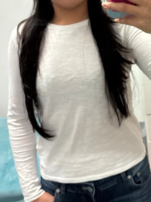 Vit långärmad topp i bomull - En enkel och stilren vit långärmad topp i mjuk bomull. Modellen har rund halsringning och en rak passform som sitter snyggt till jeans eller kjol. Perfekt basplagg för alla tillfällen och lätt att matcha med olika outfits.