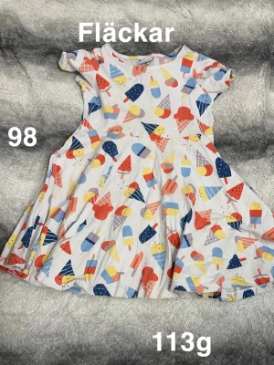 Färgglad glassmönstrad barnklänning - Supersöt klänning med glassar i olika färger på vit botten. Rund hals, korta ärmar och snurrig kjol. Perfekt för sommarens alla äventyr! 🌸 Fläckar. Storlek 98